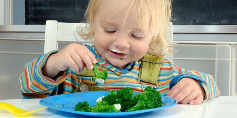 young blonde child picking up broccoli to eat