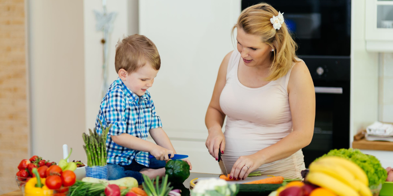 Pregnant woman cutting up vegetables with 3 year old 