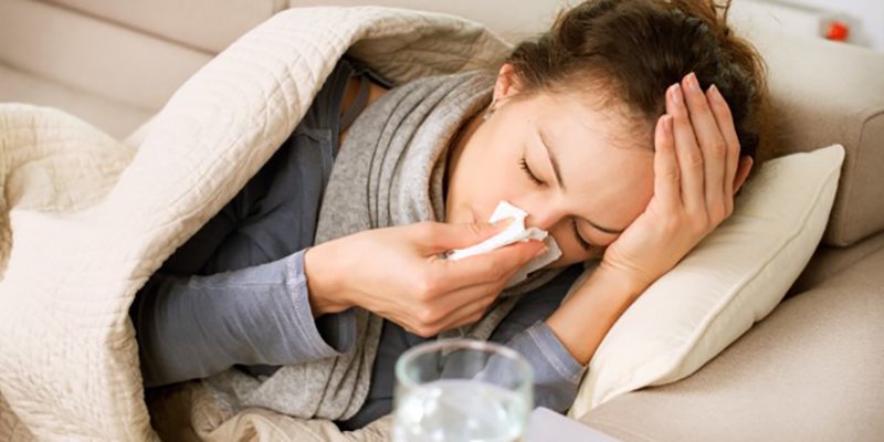 Sick woman on lounge covering nose with tissue
