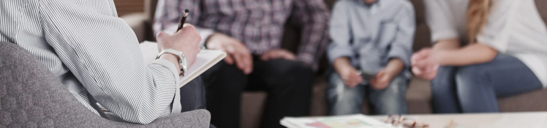 a person is taking notes while listening to a family in a counselling session